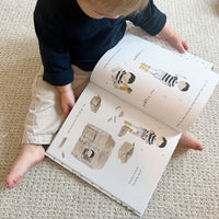 Child reading a book with illustrations of children playing on a carpeted floor.