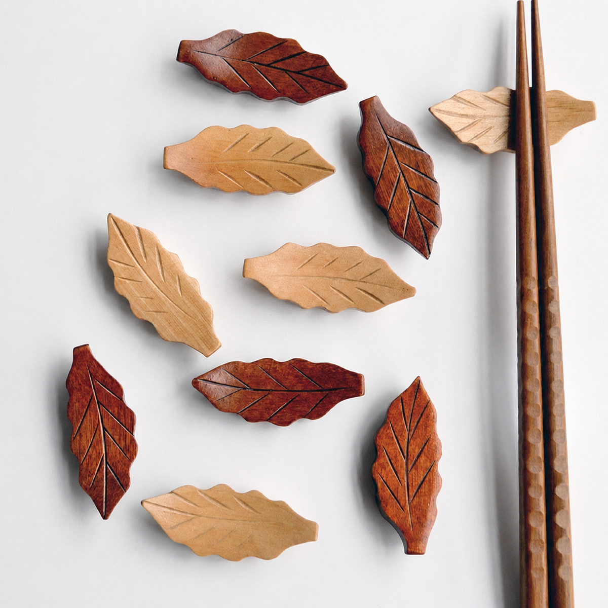 Wooden leaf-shaped coasters on a light gray background with wooden chopsticks.