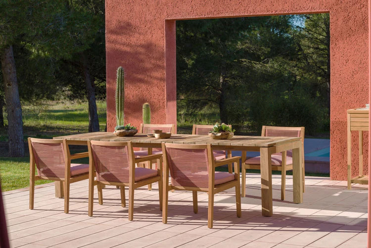 Outdoor dining set with table and chairs on a wooden deck against a red wall.