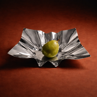 Silver wavy bowl with a green pear on a brown background