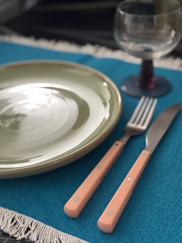 Dinner setting with green plate, pink cutlery, and glass on a blue placemat.