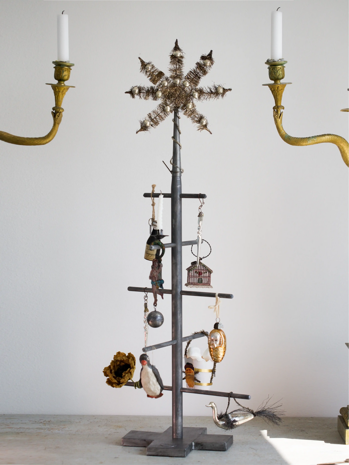 Decorative metal tree with hanging ornaments and candles on a plain background