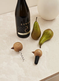 Nordic style corkscrew and wine stopper on a marble table with a bottle of wine and two pears