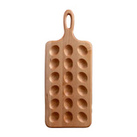 A rectangular wooden serving board with a loop handle and six oval cavities, standing upright on a wooden surface against a dark wood plank background.