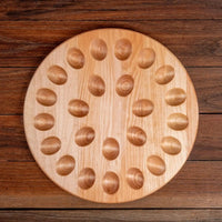 A round wooden board with twenty-four raised oval bumps, photographed from above on a dark wood plank surface.