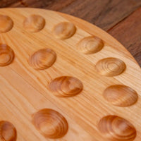 A close-up of a light natural wood round egg tray with multiple oval depressions.