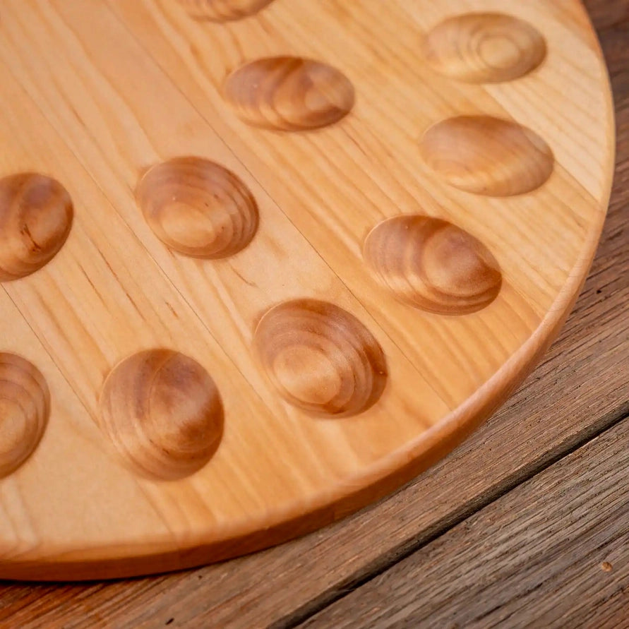A close-up of a round wooden board with oval raised nubs, resting on a rustic wooden surface.