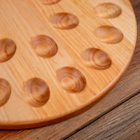 A close-up of a round wooden board with oval raised nubs, resting on a rustic wooden surface.