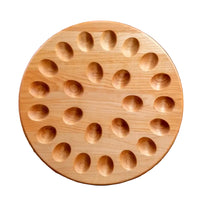 A round wooden board with multiple oval indentations, photographed standing upright against a white background