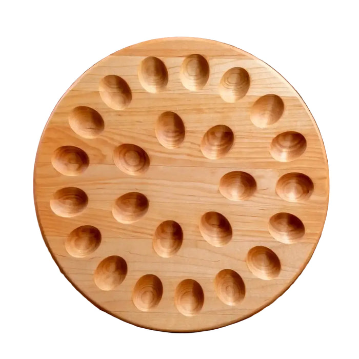 A round wooden board with multiple oval indentations, photographed standing upright against a white background