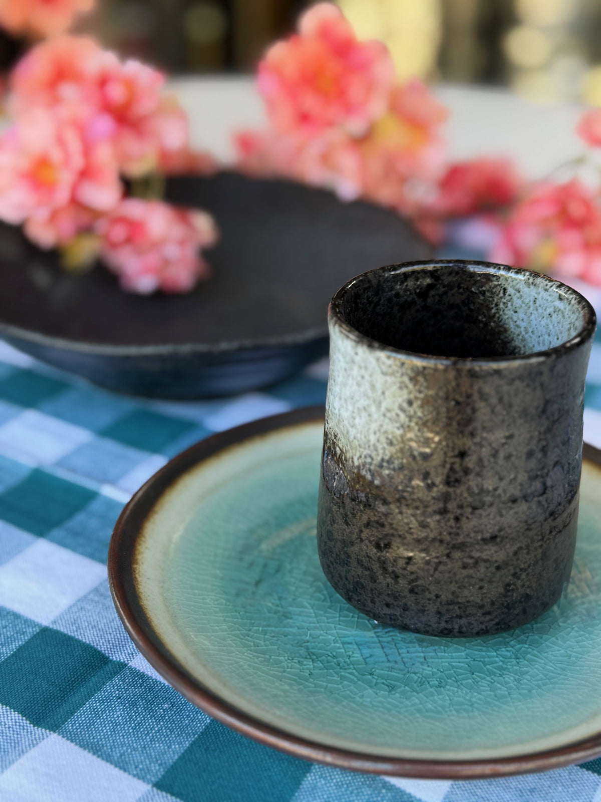Ceramic cup on a green plate with flowers in the background