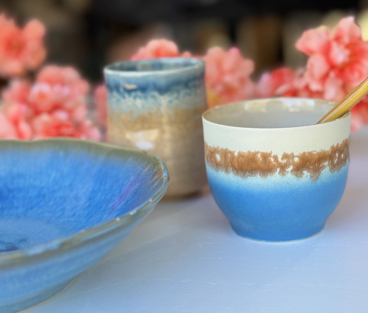 Ceramic bowls with blue and brown glaze on a white surface with pink flowers in the background.