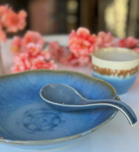 Blue ceramic plate and spoon with a blurred background of pink flowers