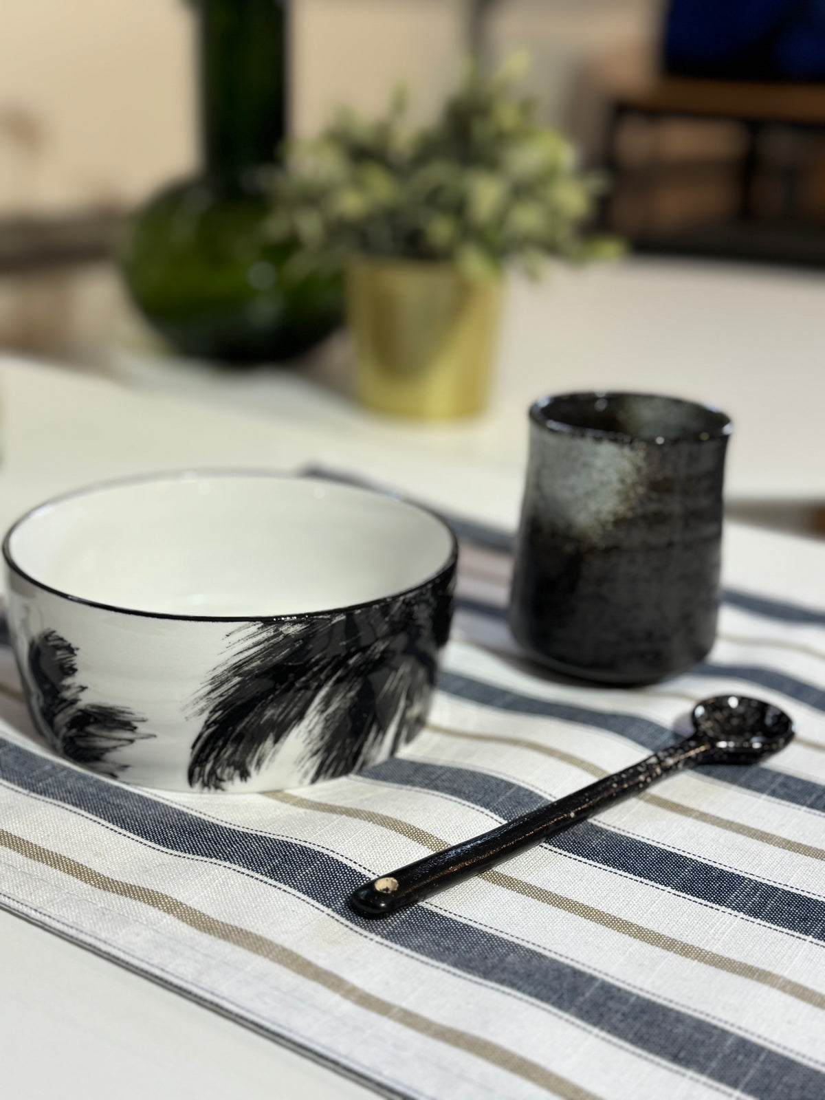 Ceramic bowl, cup, and spoon on a striped tablecloth with a blurred background