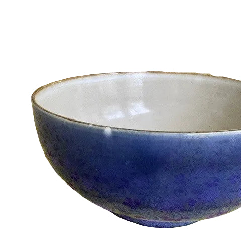 Blue ceramic bowl on a floral tablecloth with a large vase in the background
