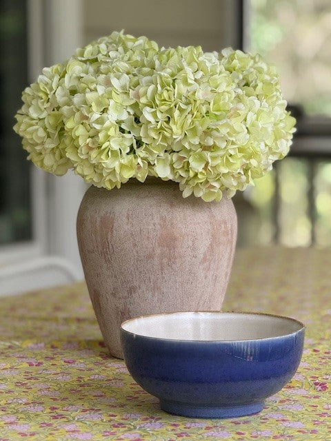 Vase with green flowers and a blue bowl on a floral tablecloth