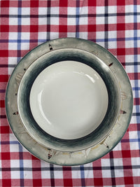 A round ceramic plate with a wide, distressed gray and black rim, shown from a top-down view on a red, white, and blue plaid tablecloth.