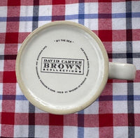 The bottom of a ceramic mug with a handle, featuring the printed brand name 'DAVID CARTER BROWN COLLECTION' on a red, white, and blue plaid fabric background.