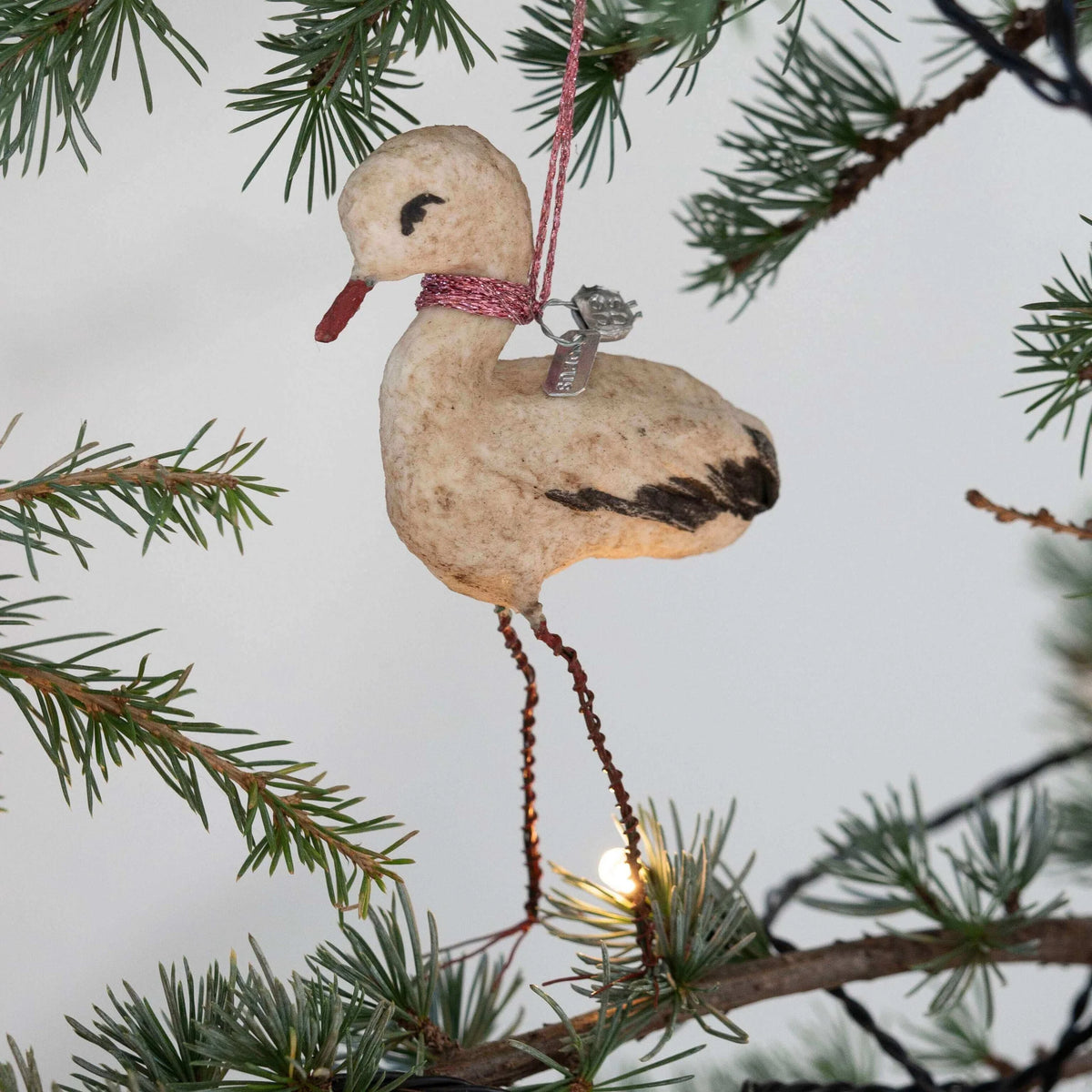 Decorative stork ornament hanging on a Christmas tree branch.