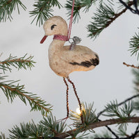 Decorative stork ornament hanging on a Christmas tree branch.