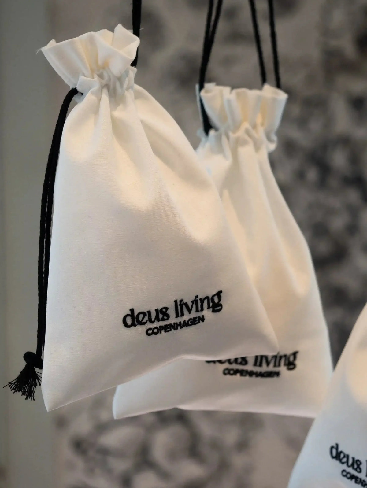 White drawstring bags with 'deus living Copenhagen' branding on a blurred background