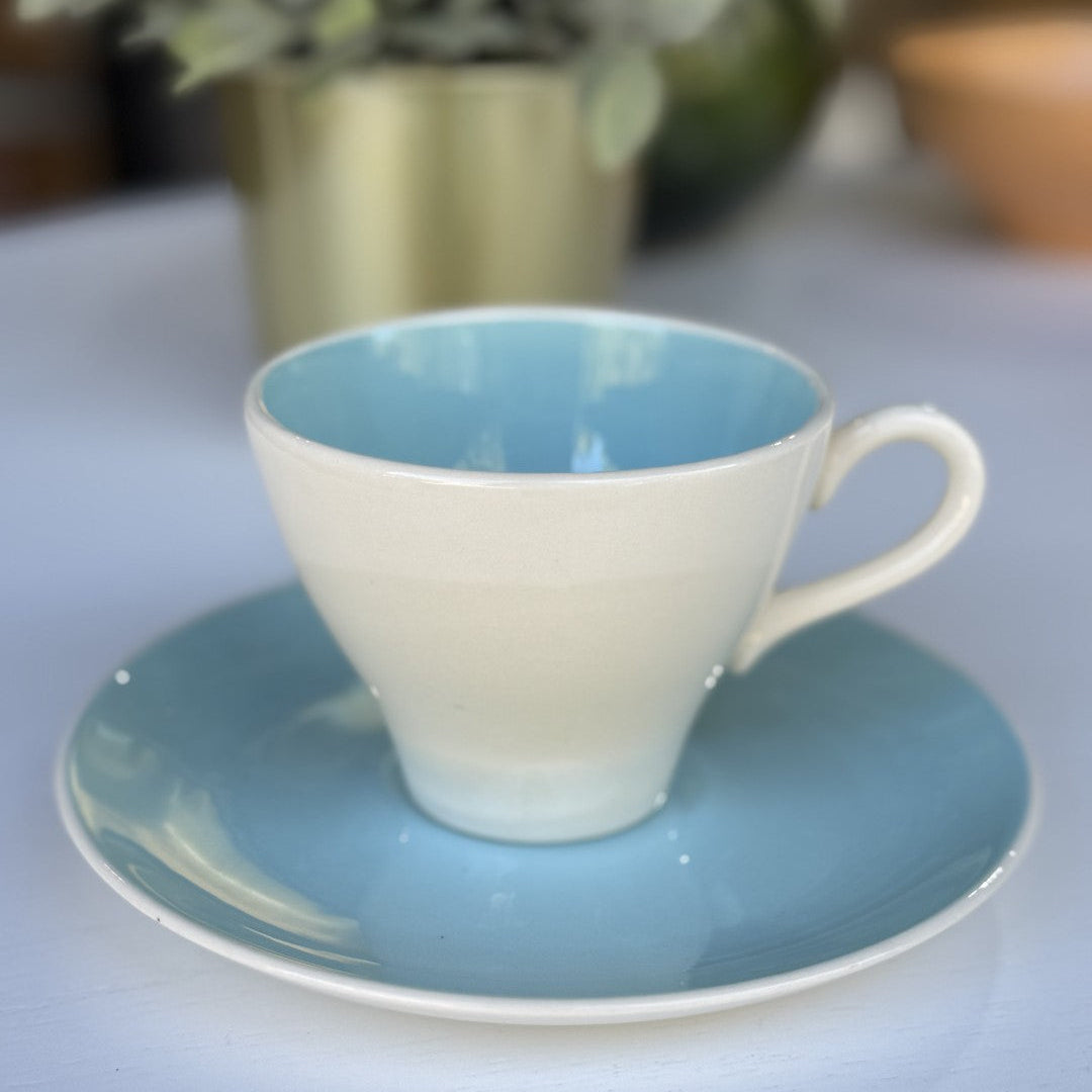 Ceramic cup and saucer with blue interior and exterior on a light surface.