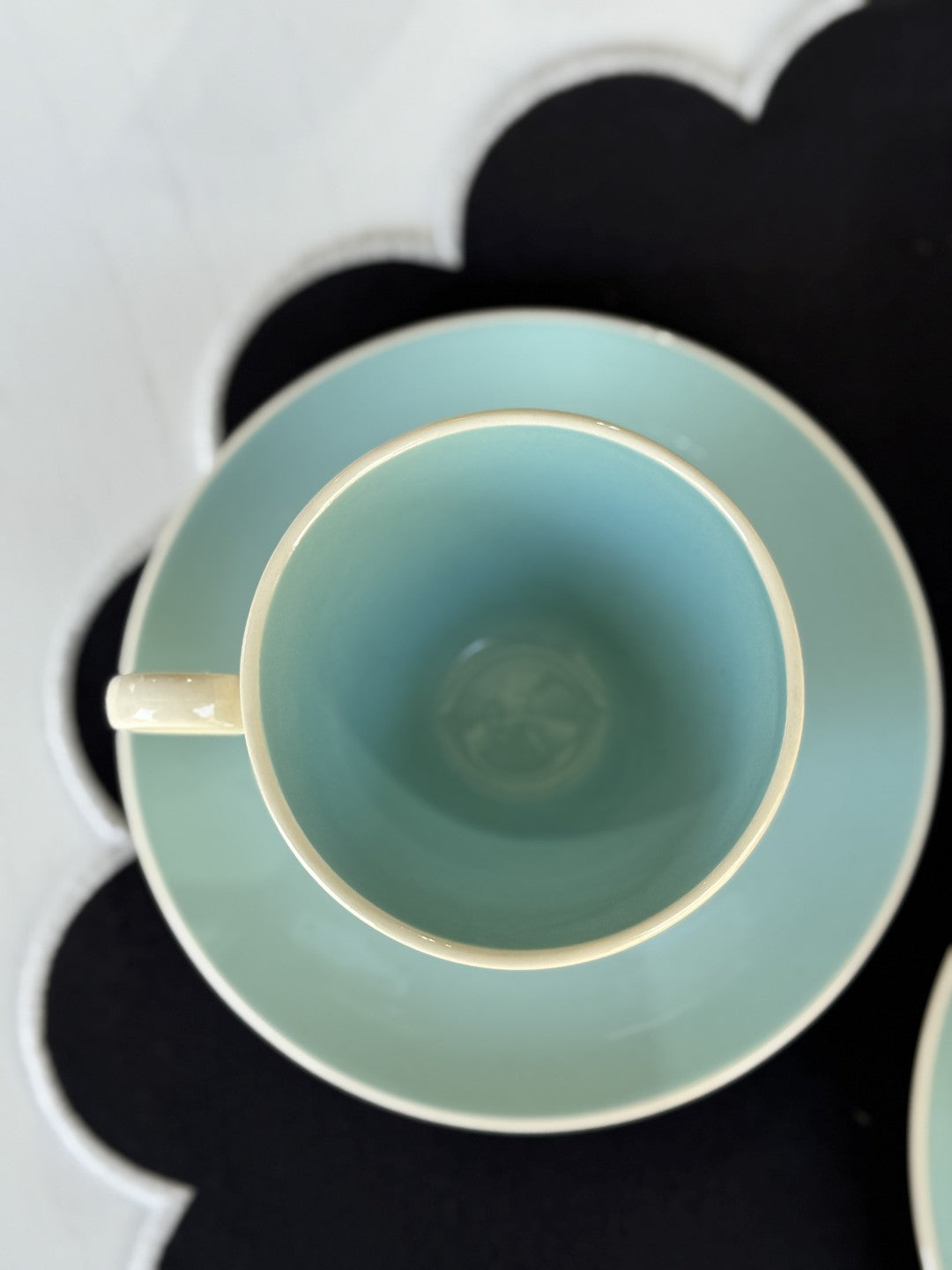 Teal cup with gold rim on a matching saucer against a black background