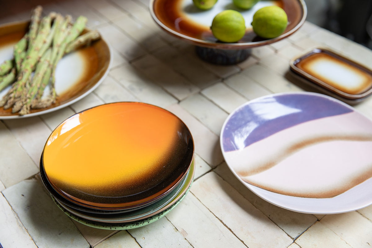 Stack of colorful ceramic plates on a wooden table with asparagus and lime.