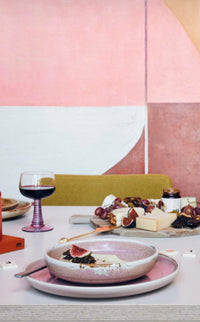 Dining table setting with plates, glasses, and fruits against a geometric wall.