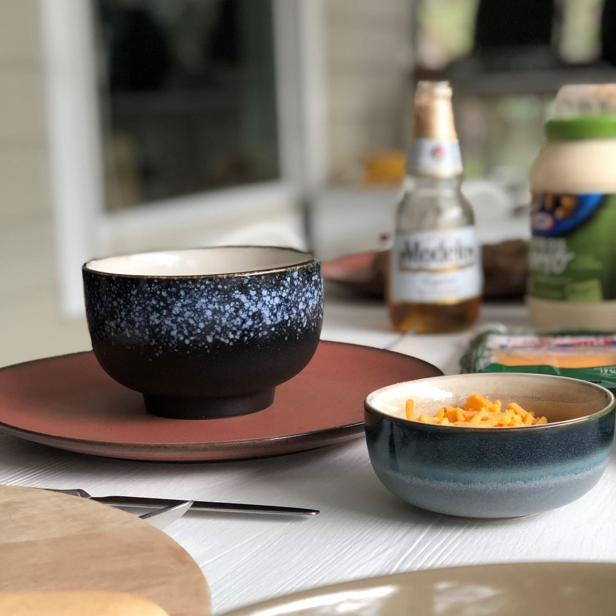 Dinner table setting with bowls, a bottle, and a jar on a blurred background