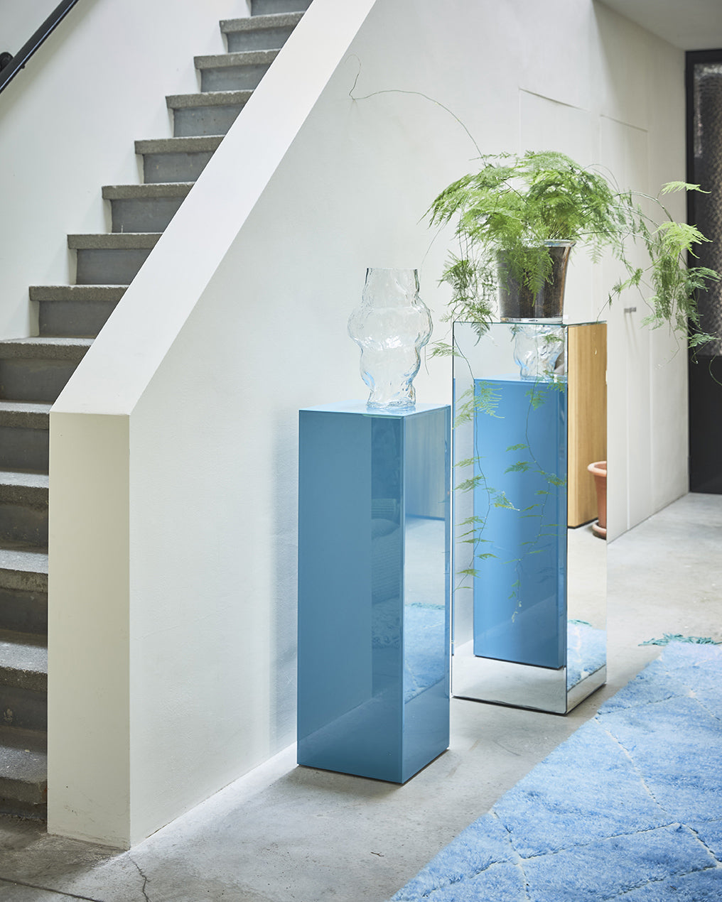 Modern interior with mirrored blue columns and plants near a staircase.