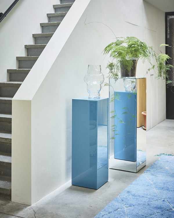 Modern interior with mirrored blue columns and plants near a staircase.