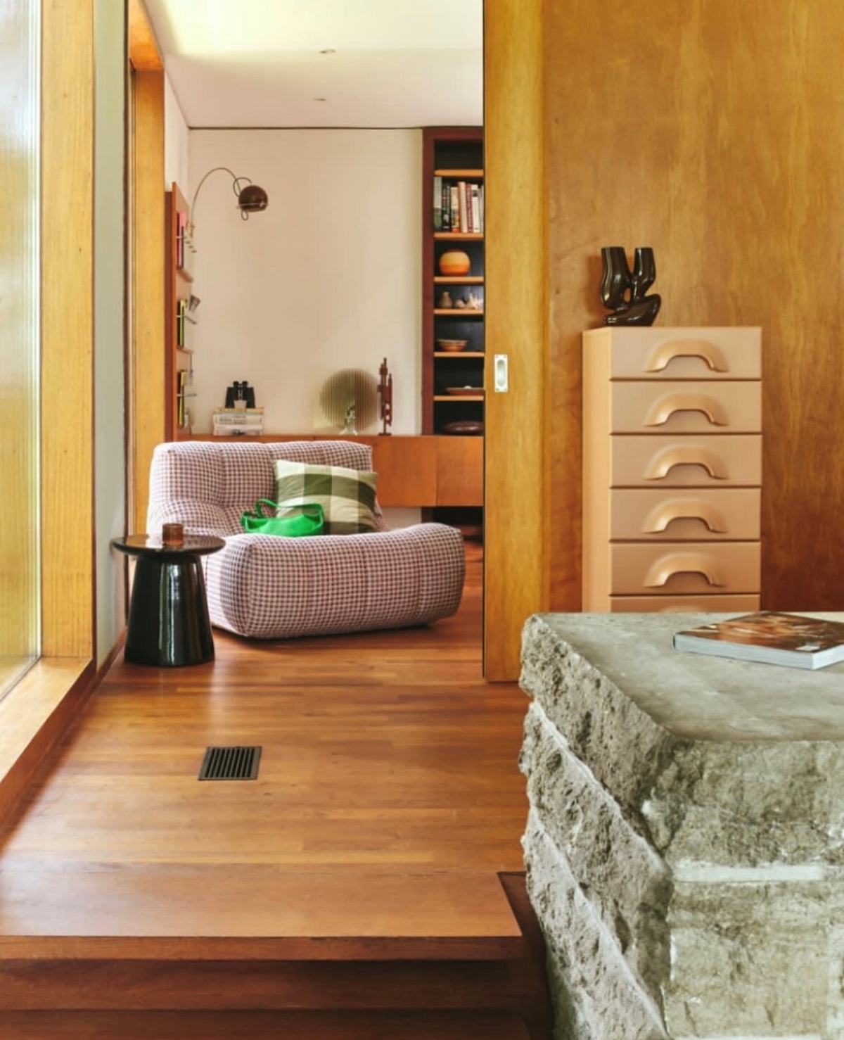 living room with wooden floor and wooden panels on wall with checkered lounge chair with green pillow and green purse