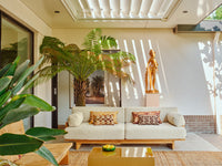 teak wooden outdoor sofa on patio with brown toned throw pillows palm tree and sculpture