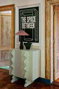 Decorative cabinet with a lamp and vase against a wall with a framed poster.