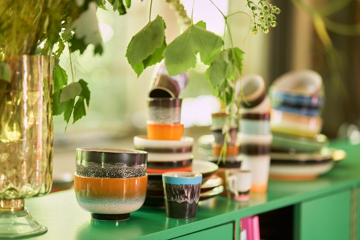 Colorful ceramic cups and bowls on a green surface with plants in the background