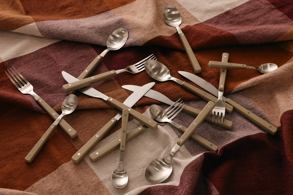 Set of silver cutlery including forks, knives, and spoons on a plaid fabric background.