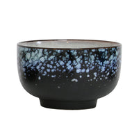 Black ceramic bowl with blue speckled pattern on a white background