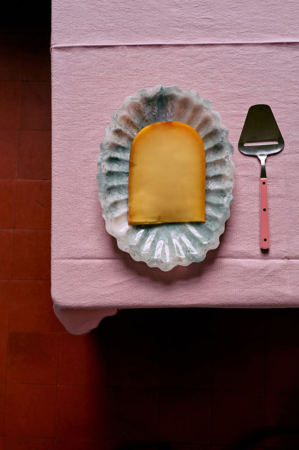 Rectangular piece of cheese on a decorative plate with a pink cheese slider on a pink surface.