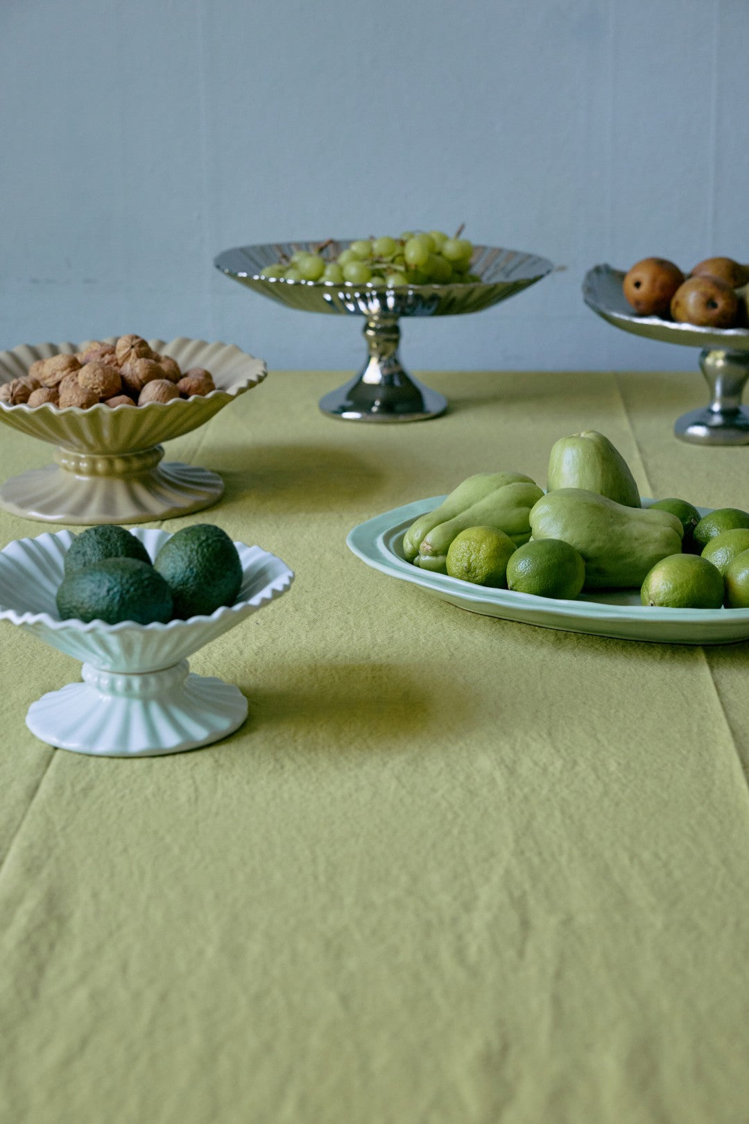 Table with various fruits including apples and limes on a light green tablecloth.