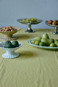 Table with various fruits including apples and limes on a light green tablecloth.