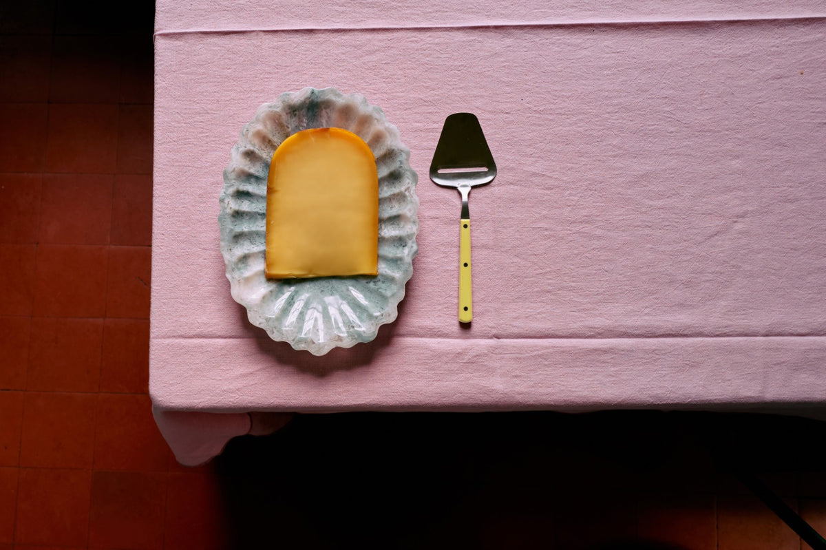 Cheese on a paper doily with a cheese knife on a pink surface