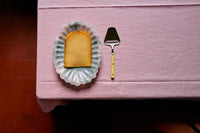 Cheese on a paper doily with a cheese knife on a pink surface