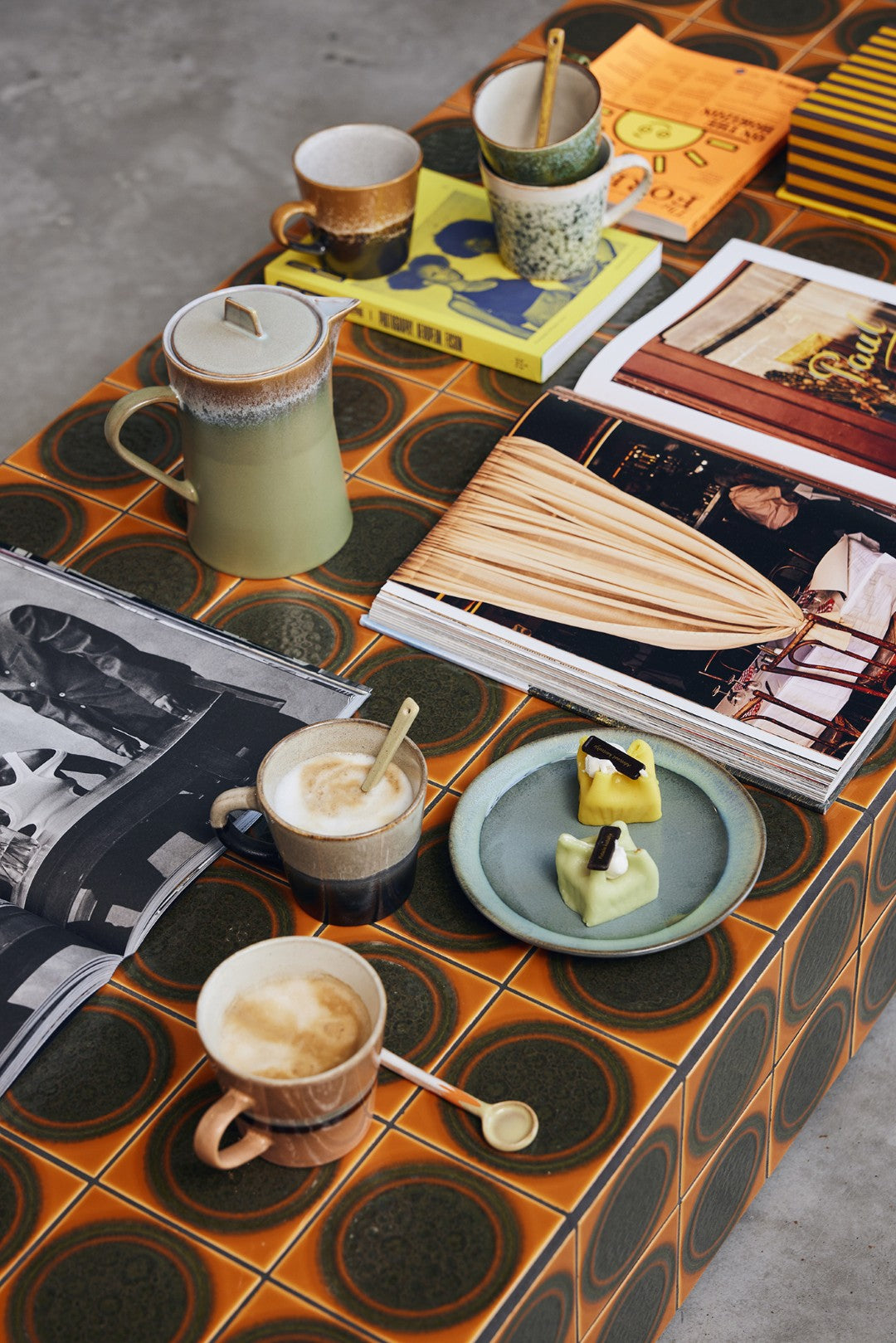 Café setting with coffee cups, a plate of pastries, and books on a tiled table.