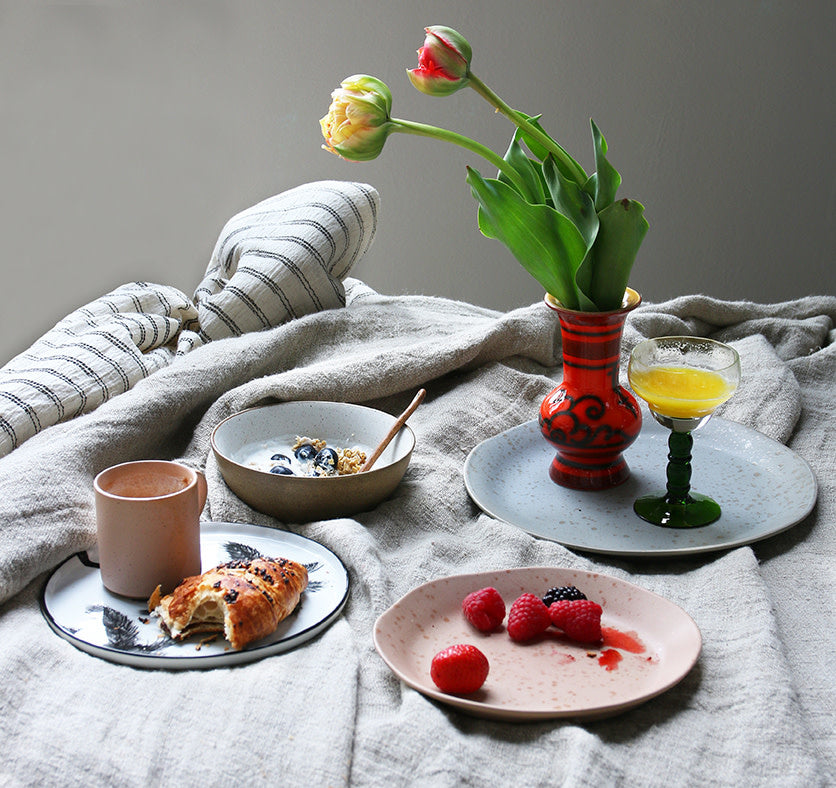 Breakfast setting with plates of food, a vase with flowers, and a glass on a textured surface.