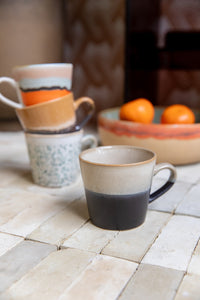 Three ceramic mugs on a tiled surface with a blurred background