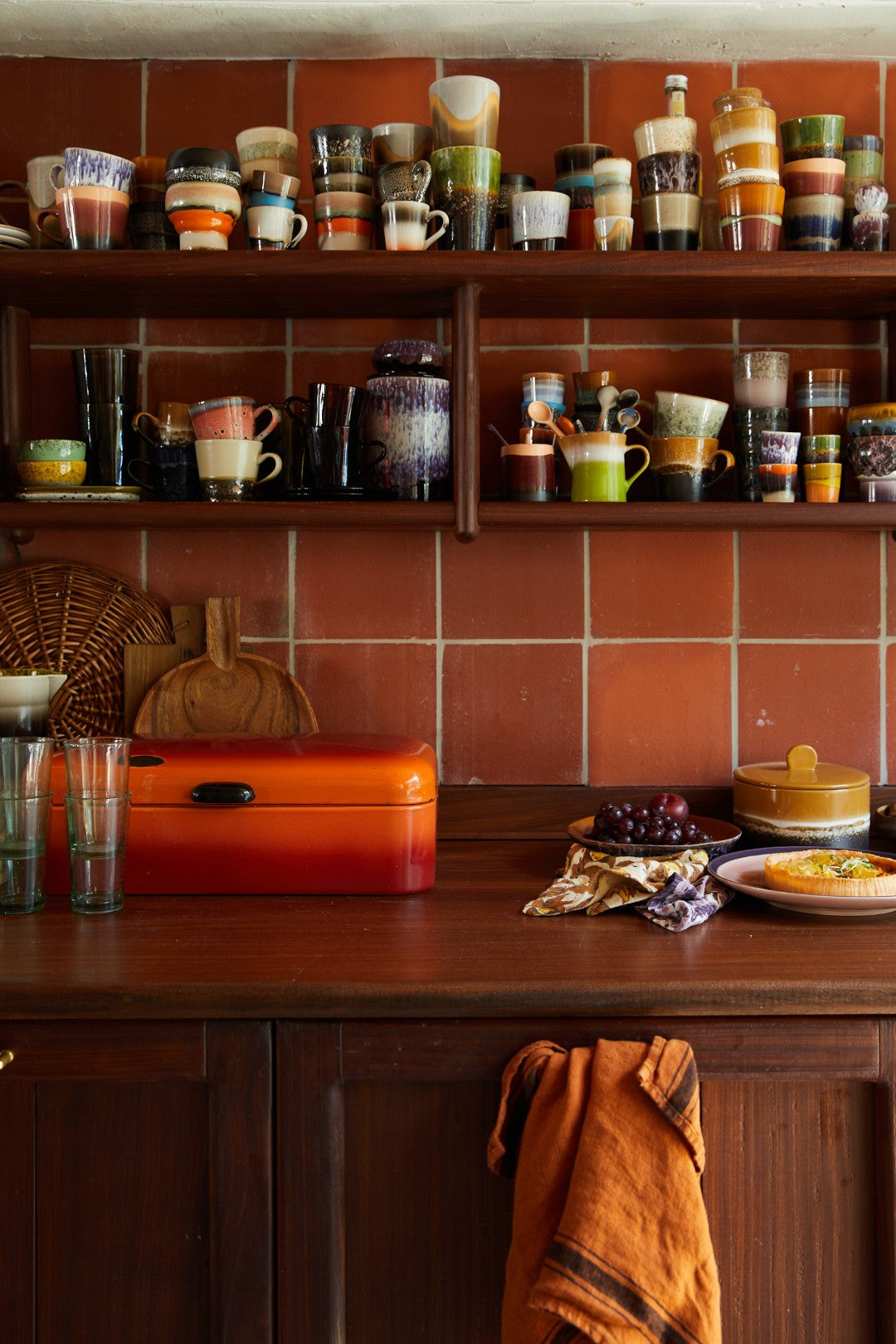 Kitchen shelf with various cups and a red toolbox on a wooden counter.