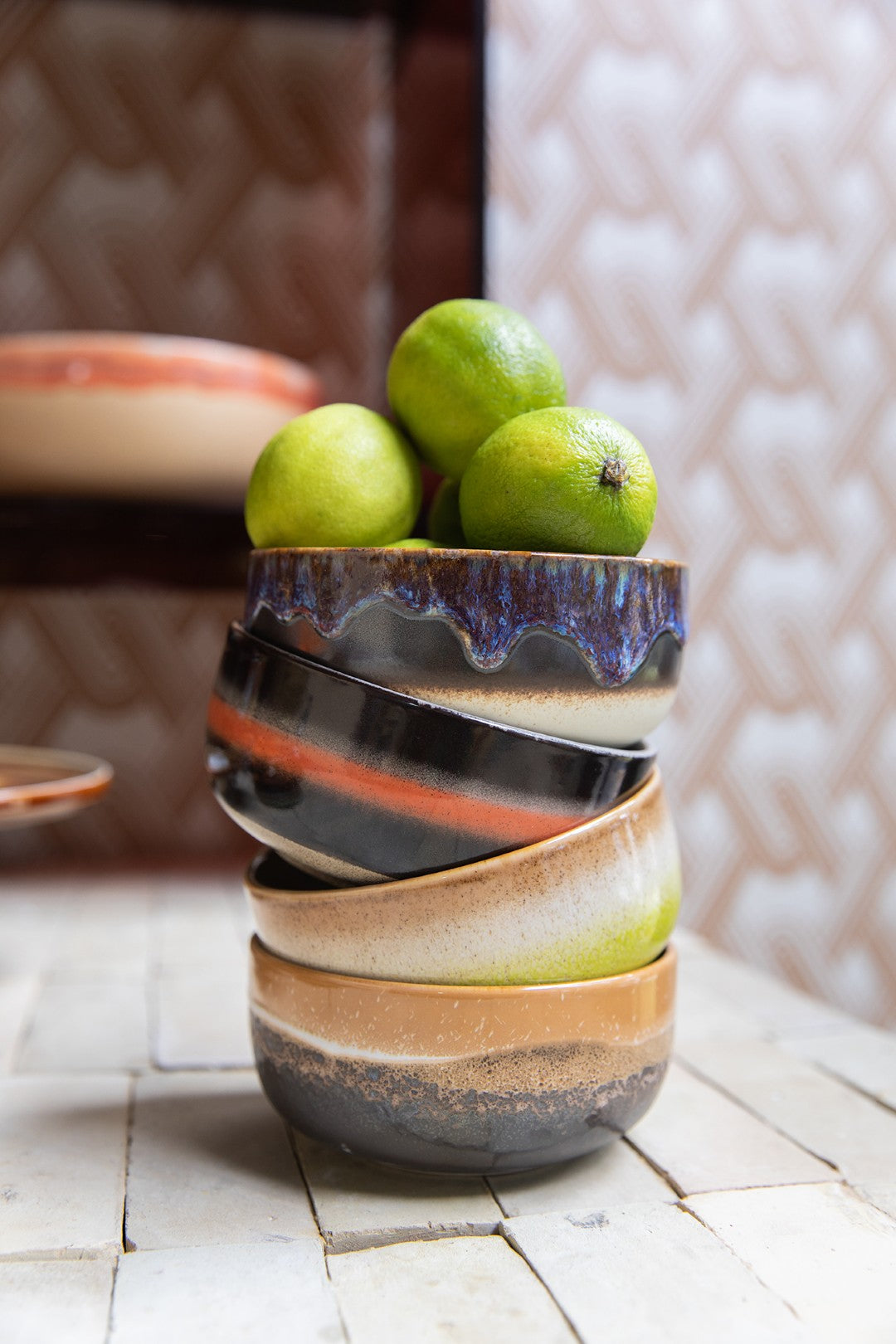 Stack of ceramic bowls with a colorful glaze holding limes on a textured surface.