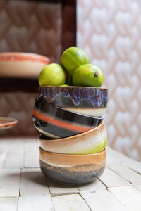 Stack of ceramic bowls with a colorful glaze holding limes on a textured surface.