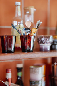 Set of colorful wooden spoons in a glass container on a kitchen shelf with blurred background